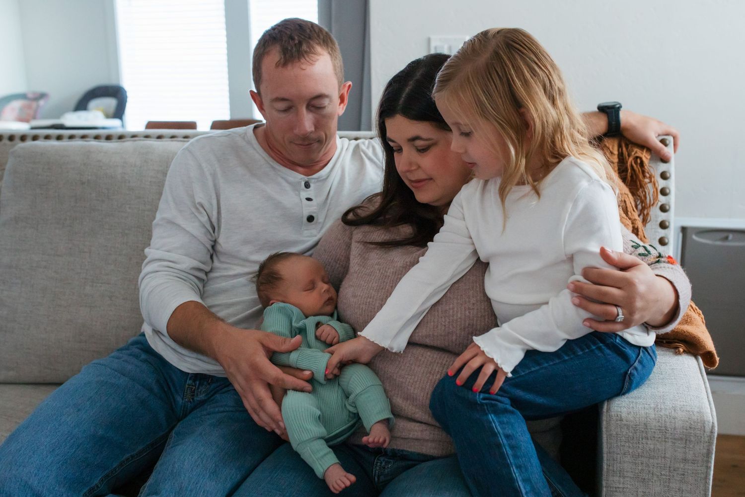 Lifestyle in-home newborn photography session in Boise, Idaho with parents and big sister cuddling their newborn baby on the couch.