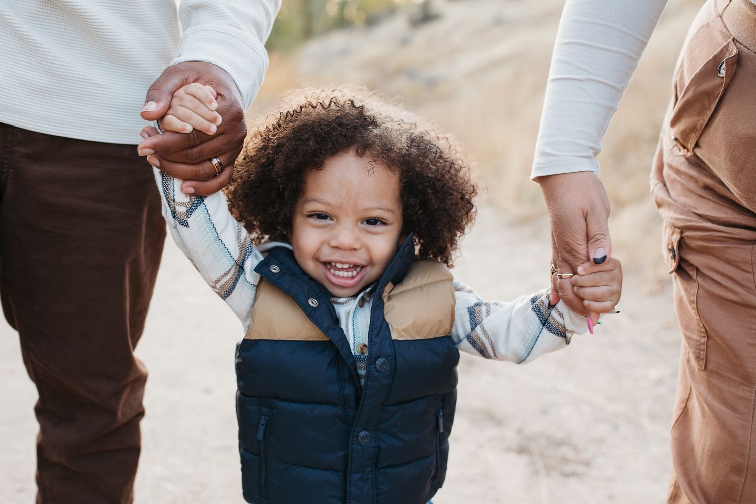 A child holds hands with adults while walking outdoors in casual clothing - lifestyle family photos in Boise