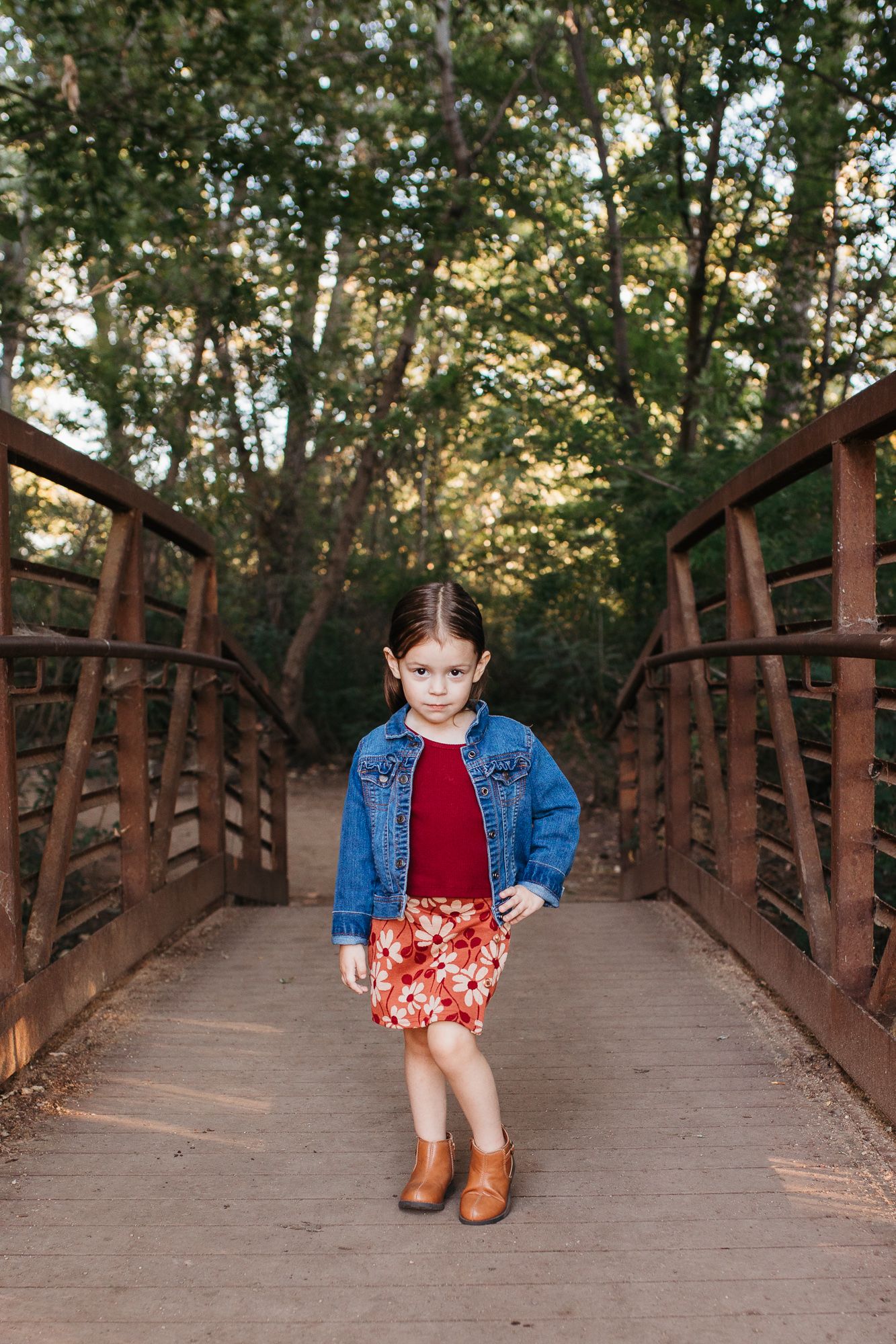 A wooden footbridge in a forest setting with someone wearing a denim jacket and floral skirt. birthday milestone photos Nampa Idaho