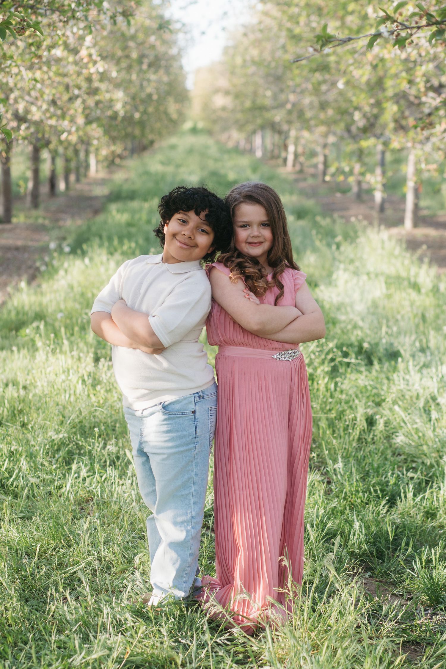 Siblings hugging and smiling in blossom orchard during spring family photo session in Caldwell Idaho