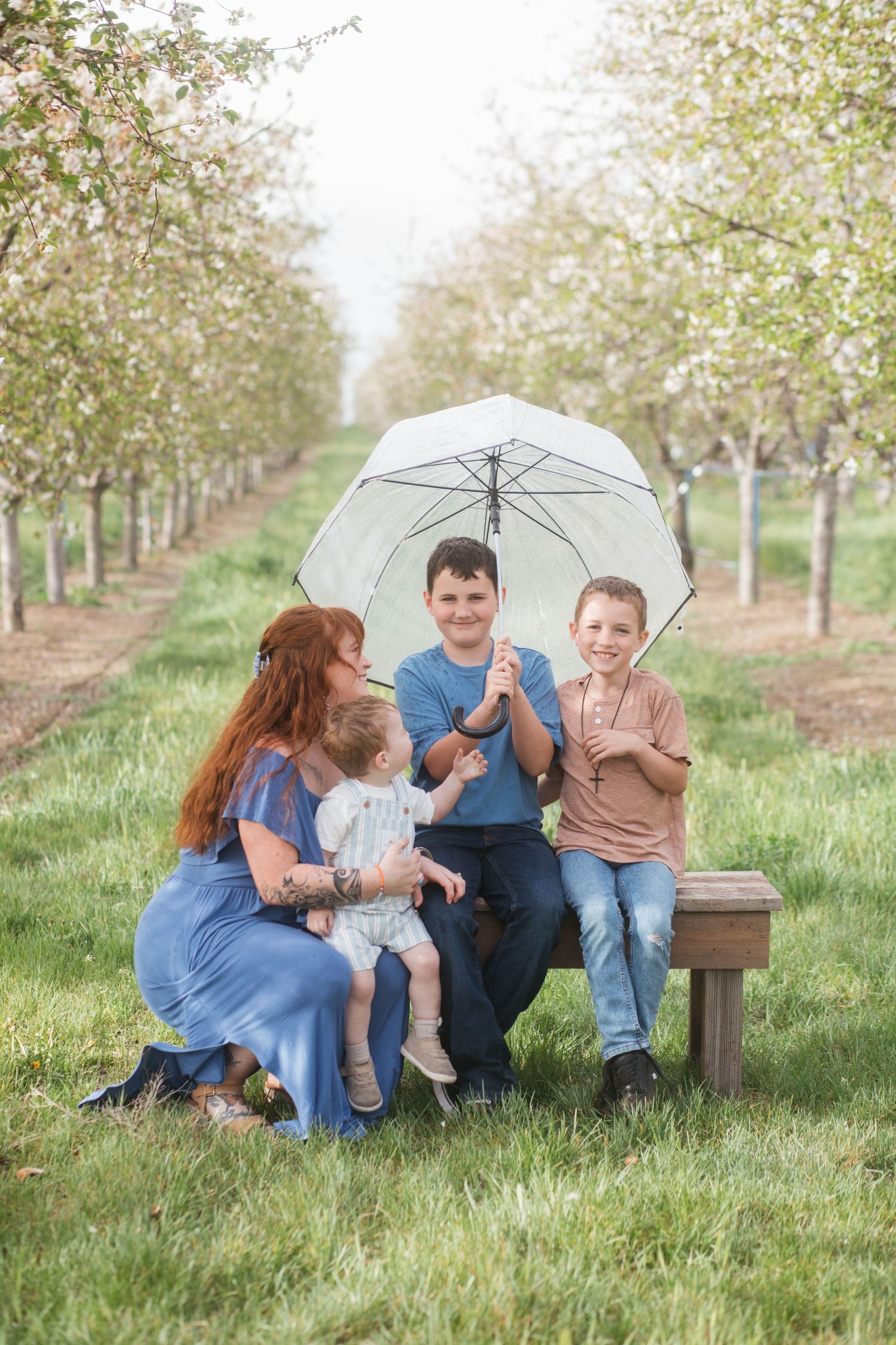 Family sitting under umbrella in cherry blossom orchard at Cherry Hill Farms in Caldwell, Idaho