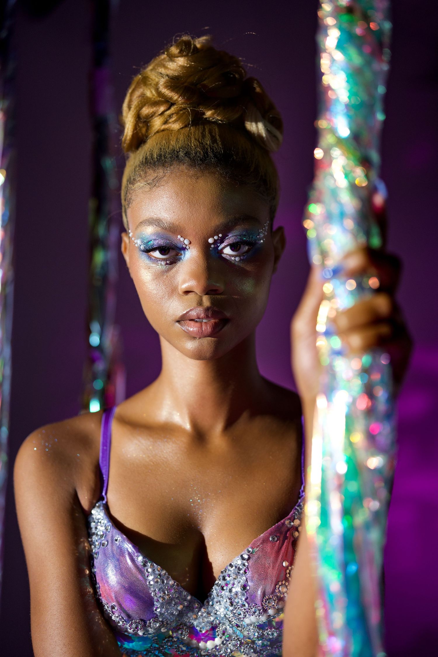 Dramatic portrait with glittery makeup and purple lighting against holographic columns.