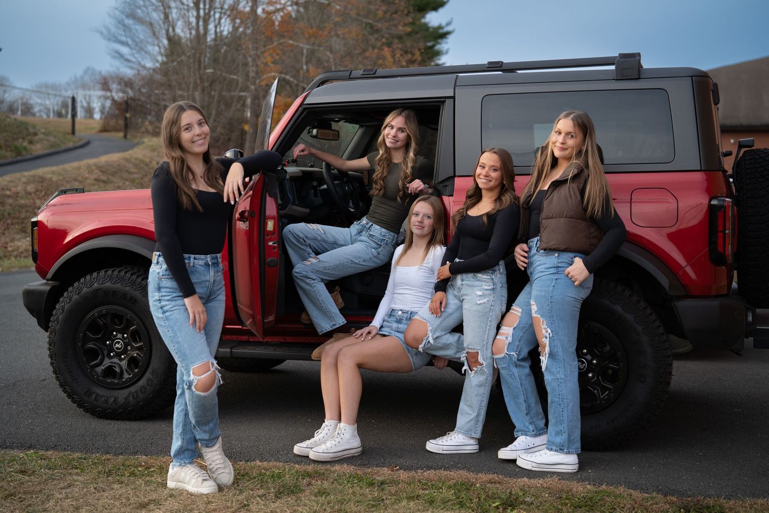 Group photo session featuring casual poses next to red trucks with lifted suspensions.