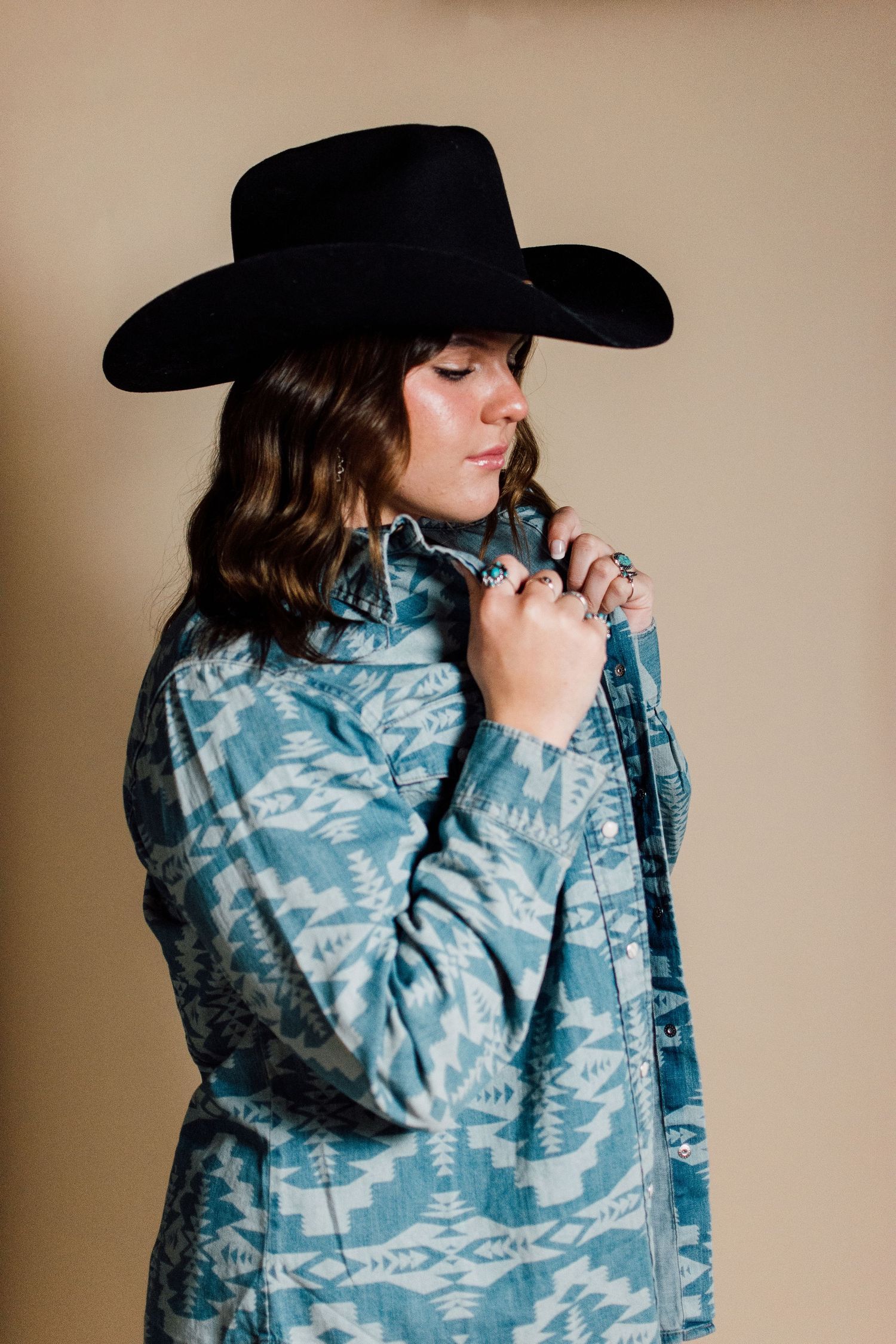 Moody portrait series in a blue patterned jacket and black cowboy hat against beige background.