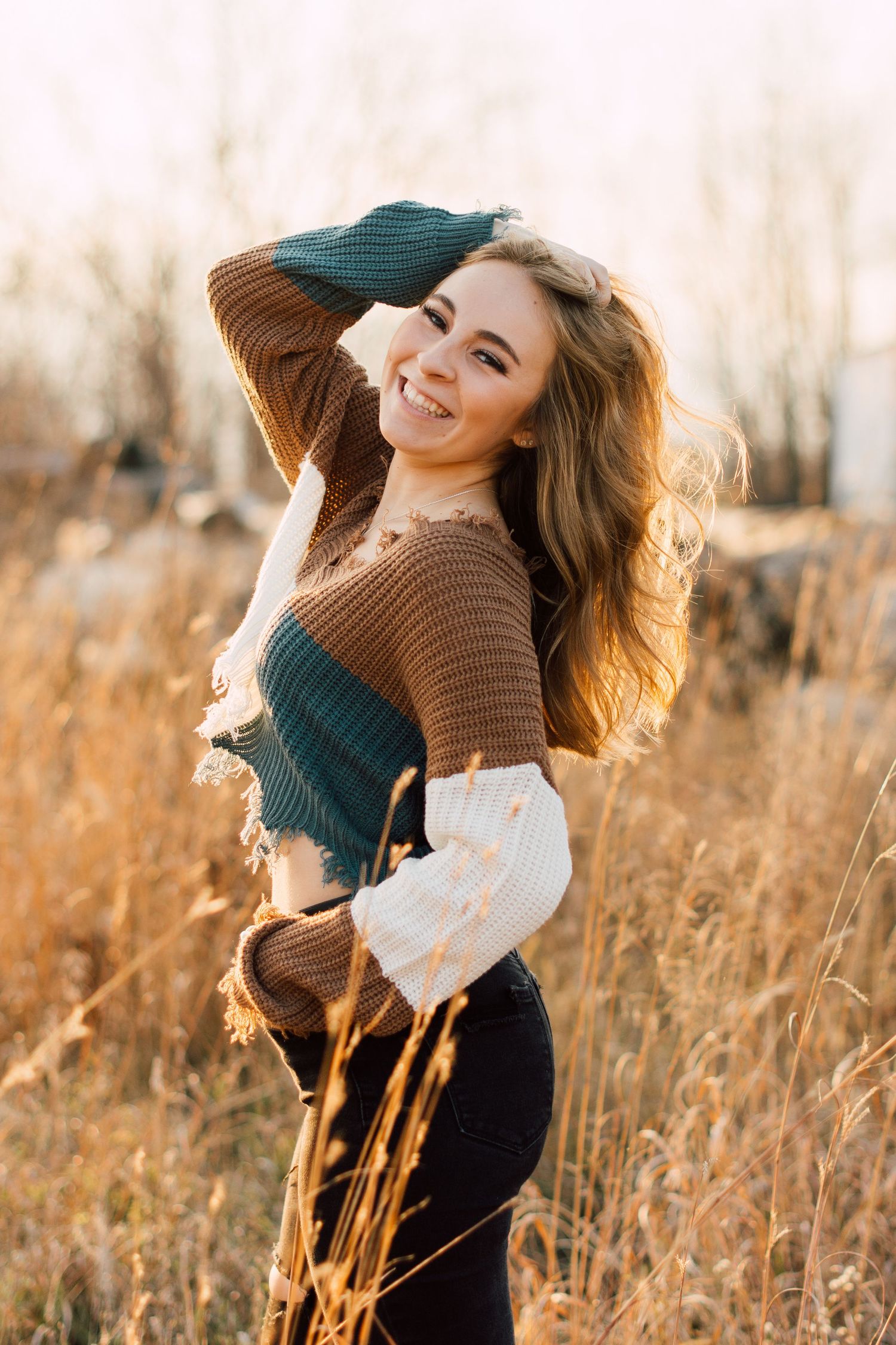 Person in brown sweater twirls playfully in autumn field at golden hour.