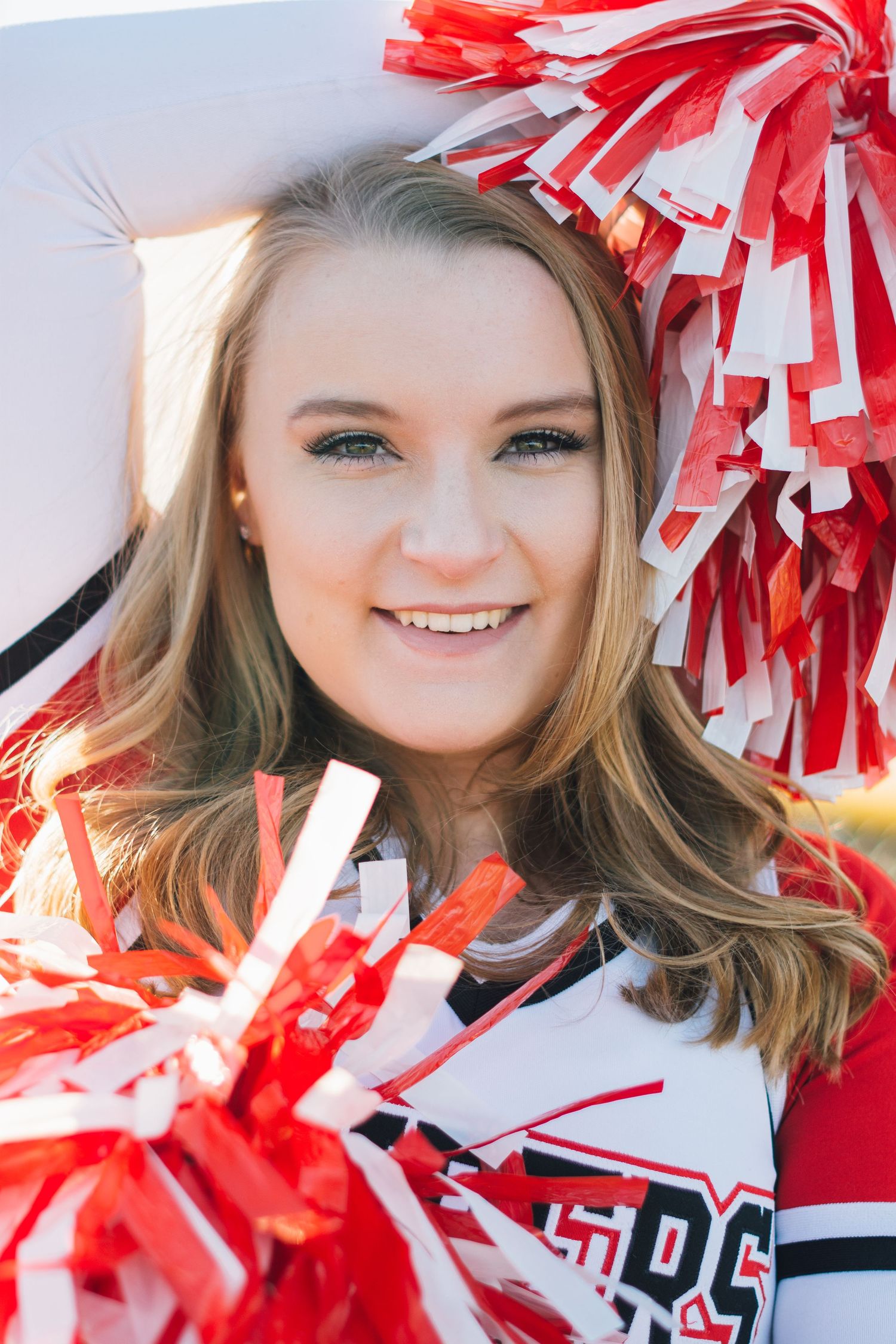 Cheerleader poses with red and white pom poms against light background.