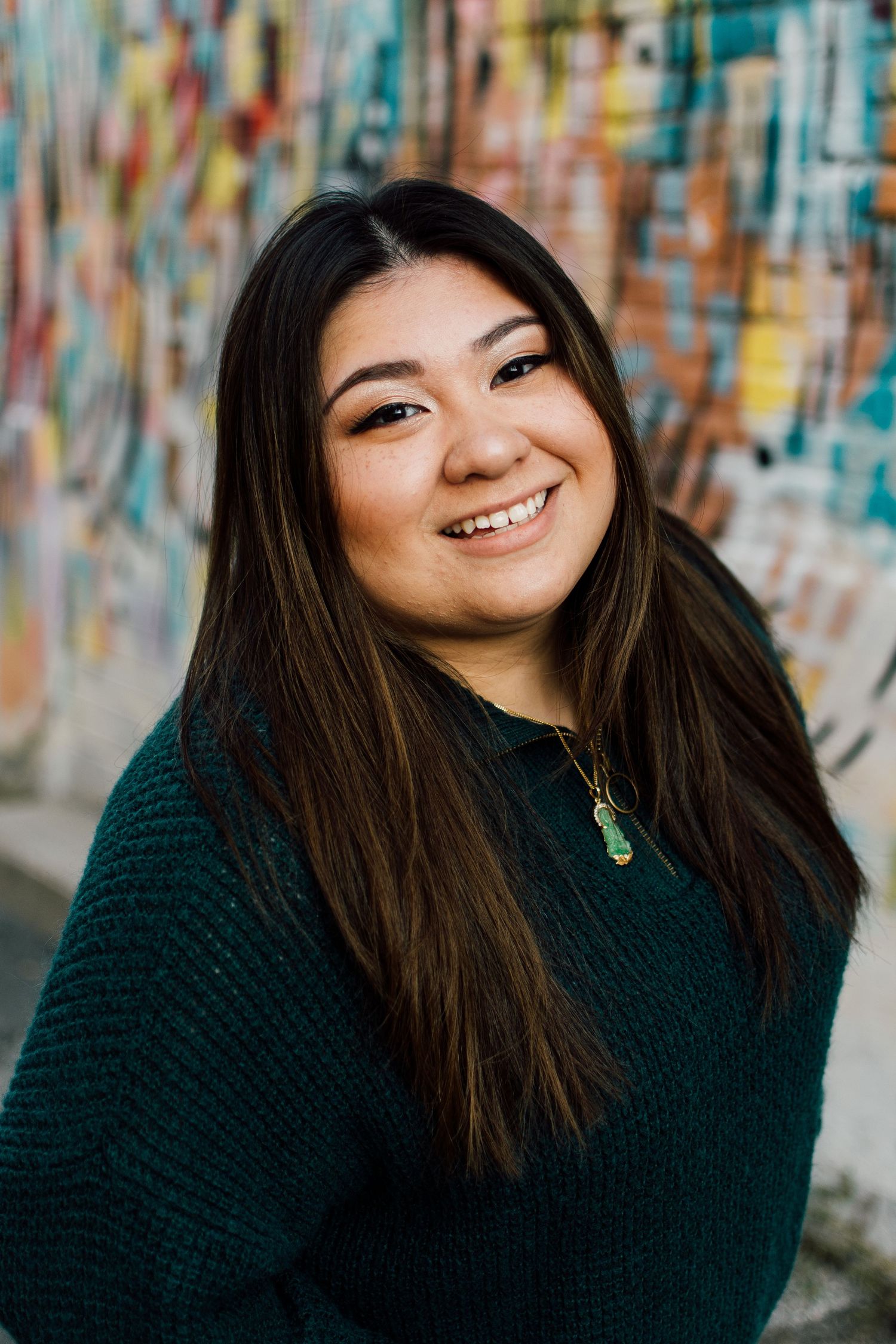 Cheerful portraits against a colorful mural wall wearing a dark green sweater.