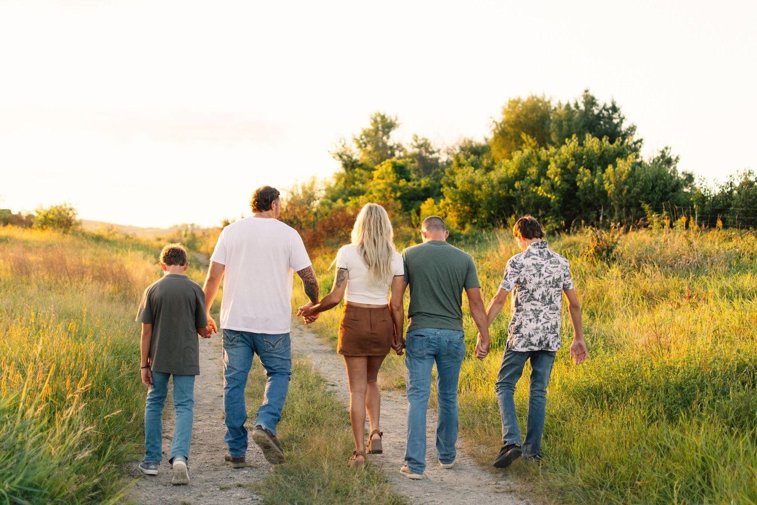 Group of people walking together through a golden sunlit meadow at sunset.
