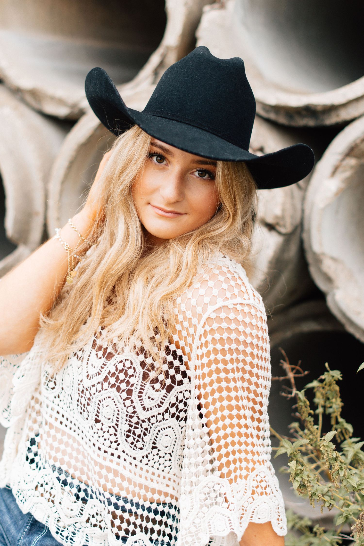 Western style portrait featuring a black cowboy hat and white lace top against a dark background.