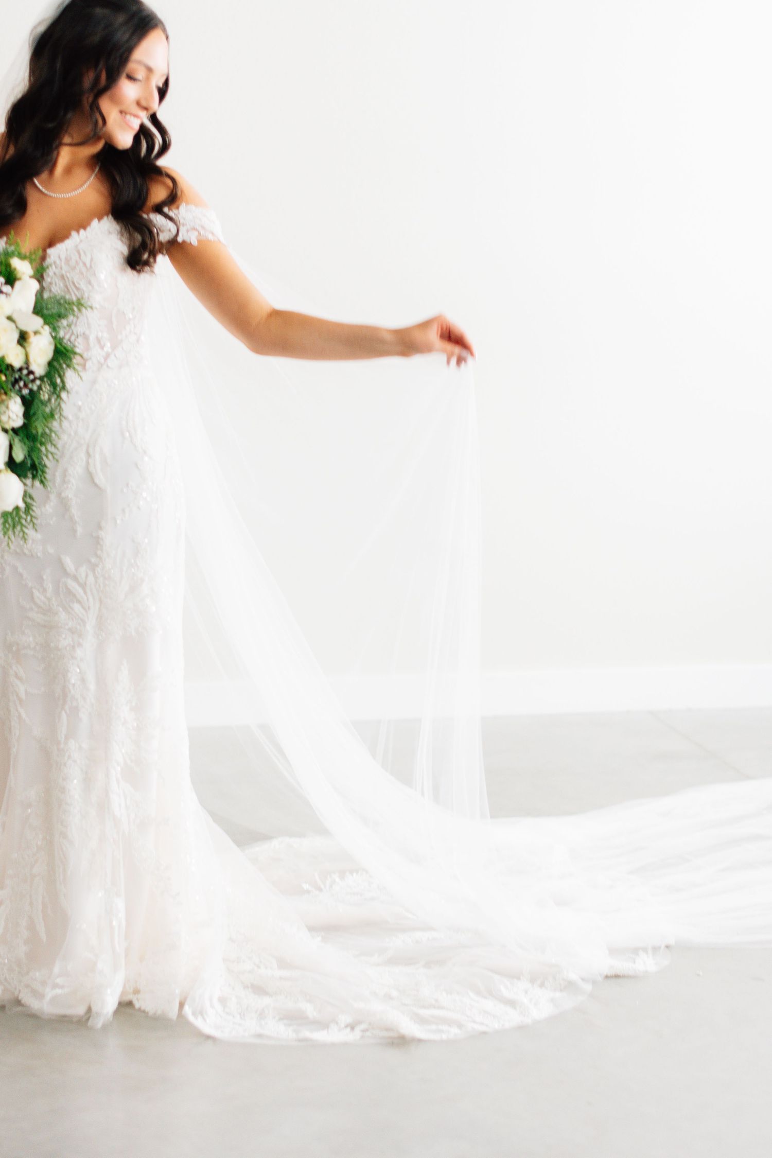 Bride in lace wedding dress twirling to show flowing train against white backdrop.