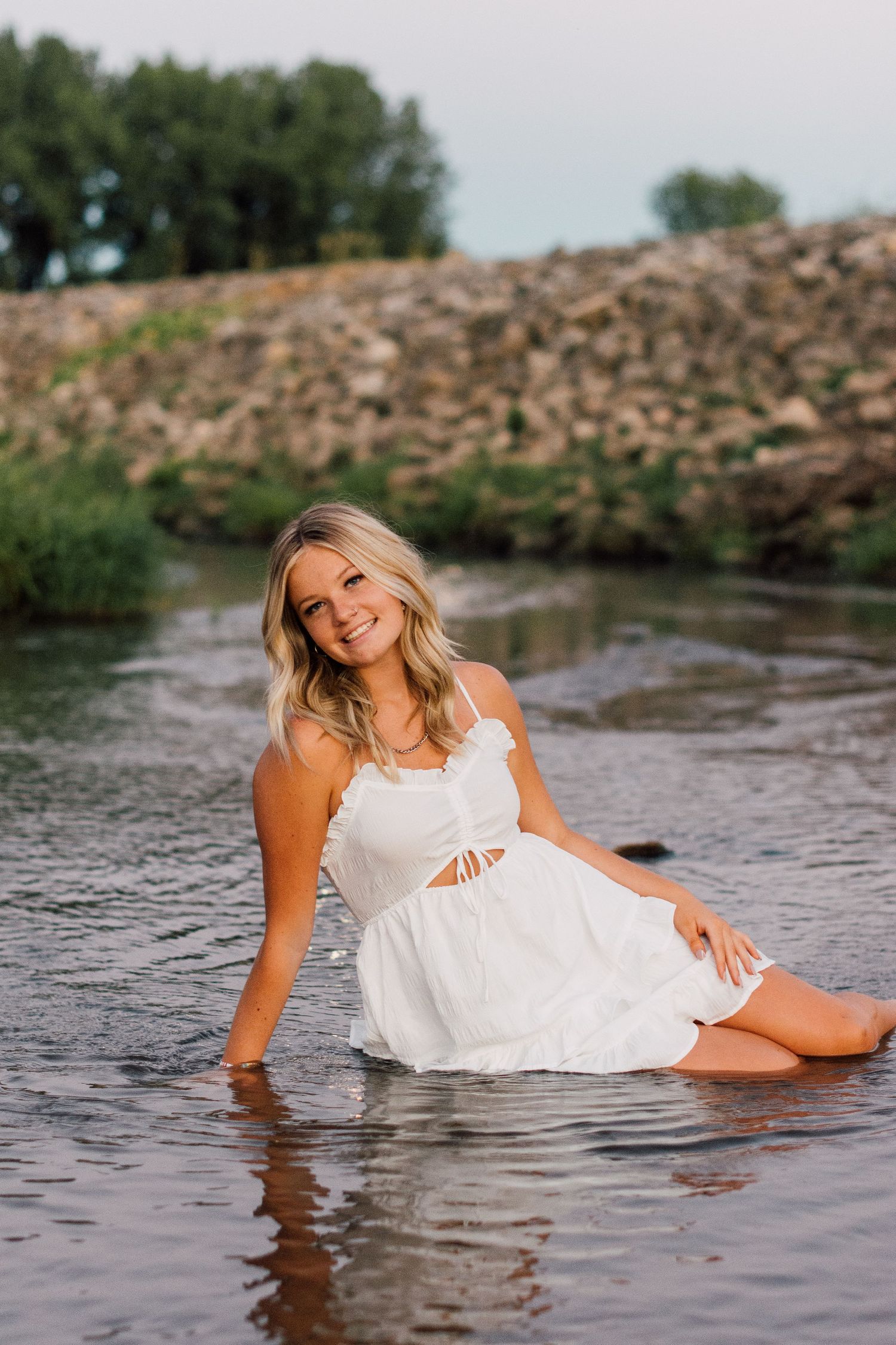 Artistic water portraits in a white dress showing playful poses by the river.