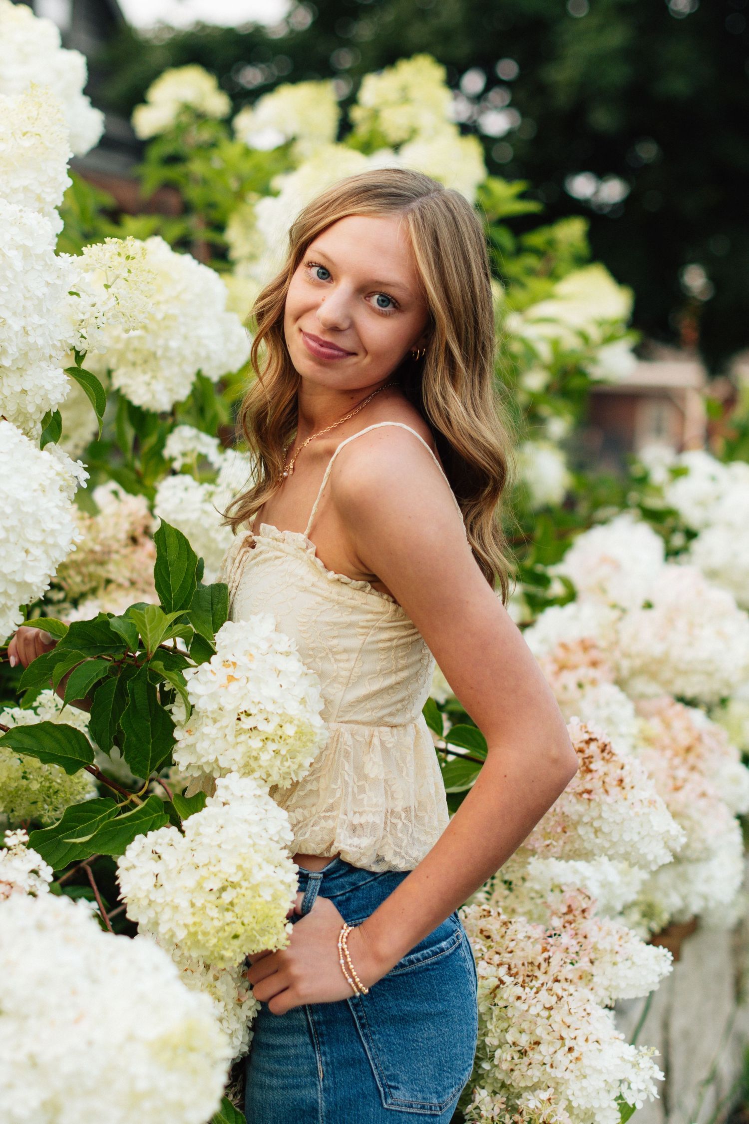 Playful summer portraits among white hydrangea blooms wearing denim and cream top.