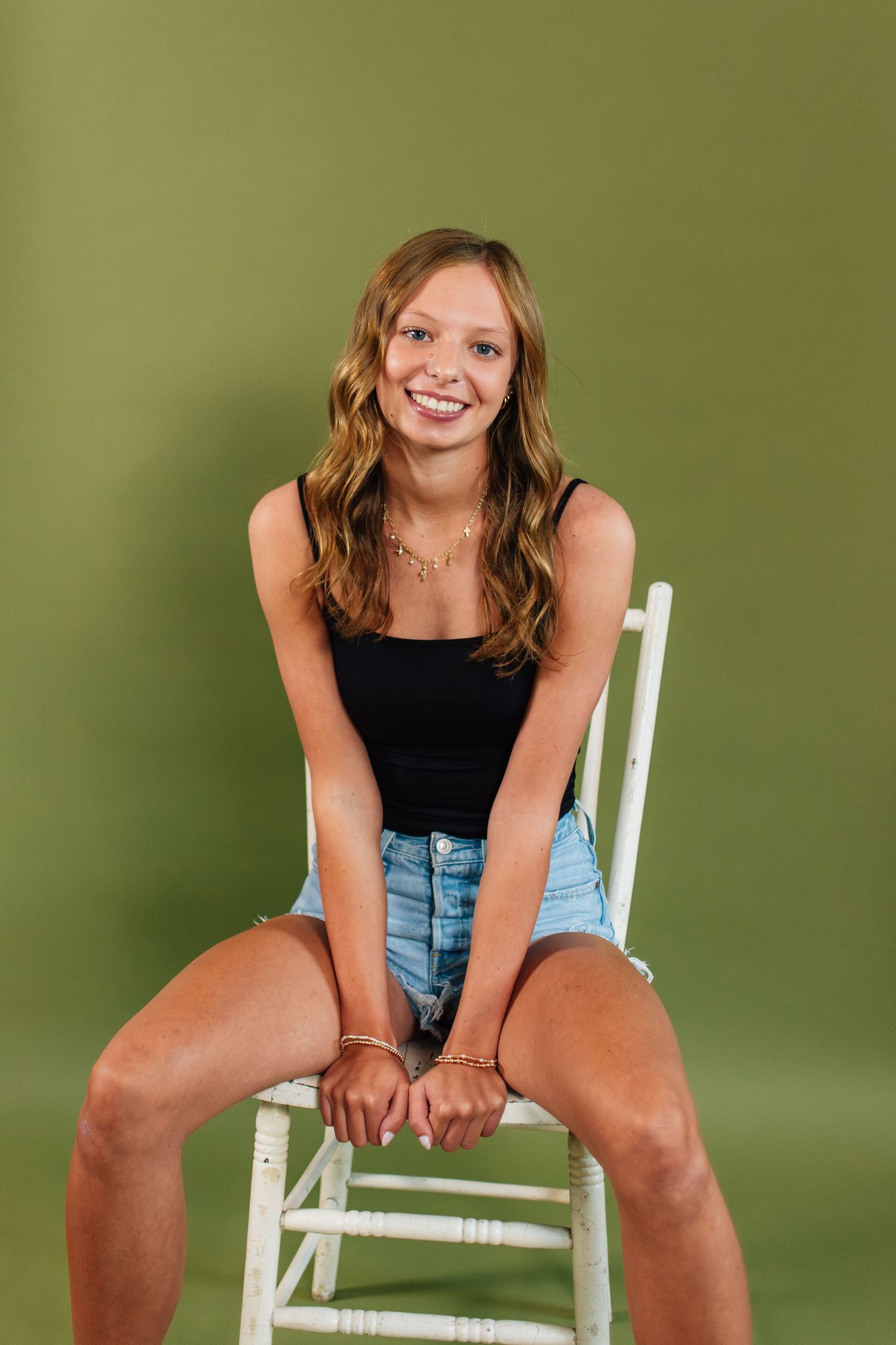 Casual portrait session with person sitting on white chair against green background.