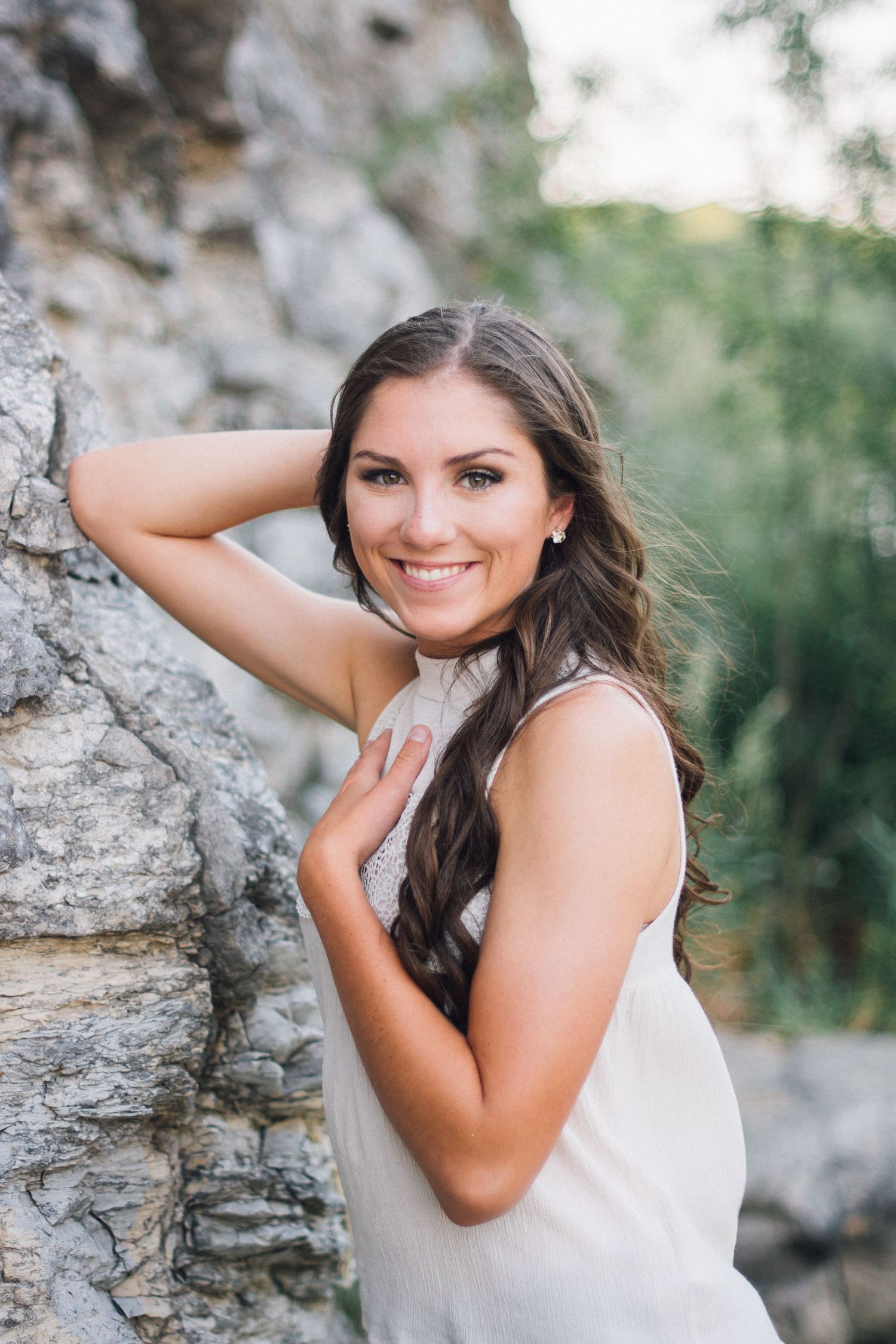Woman in white tank top poses against textured rock wall in outdoor portrait session.