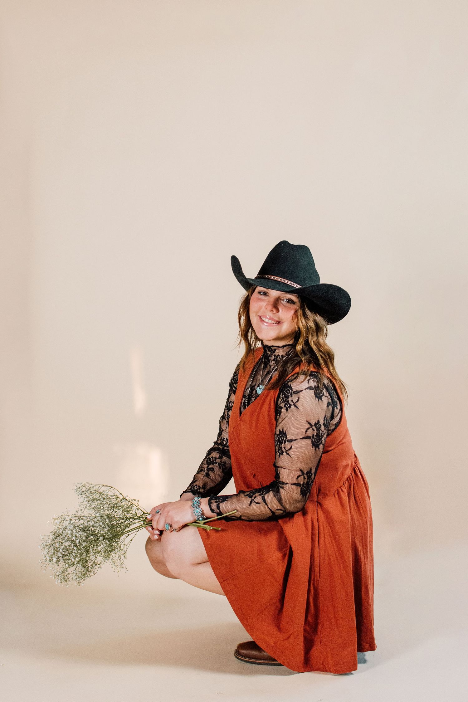 Western-inspired photoshoot featuring a rust dress, black cowboy hat, and dried flowers.