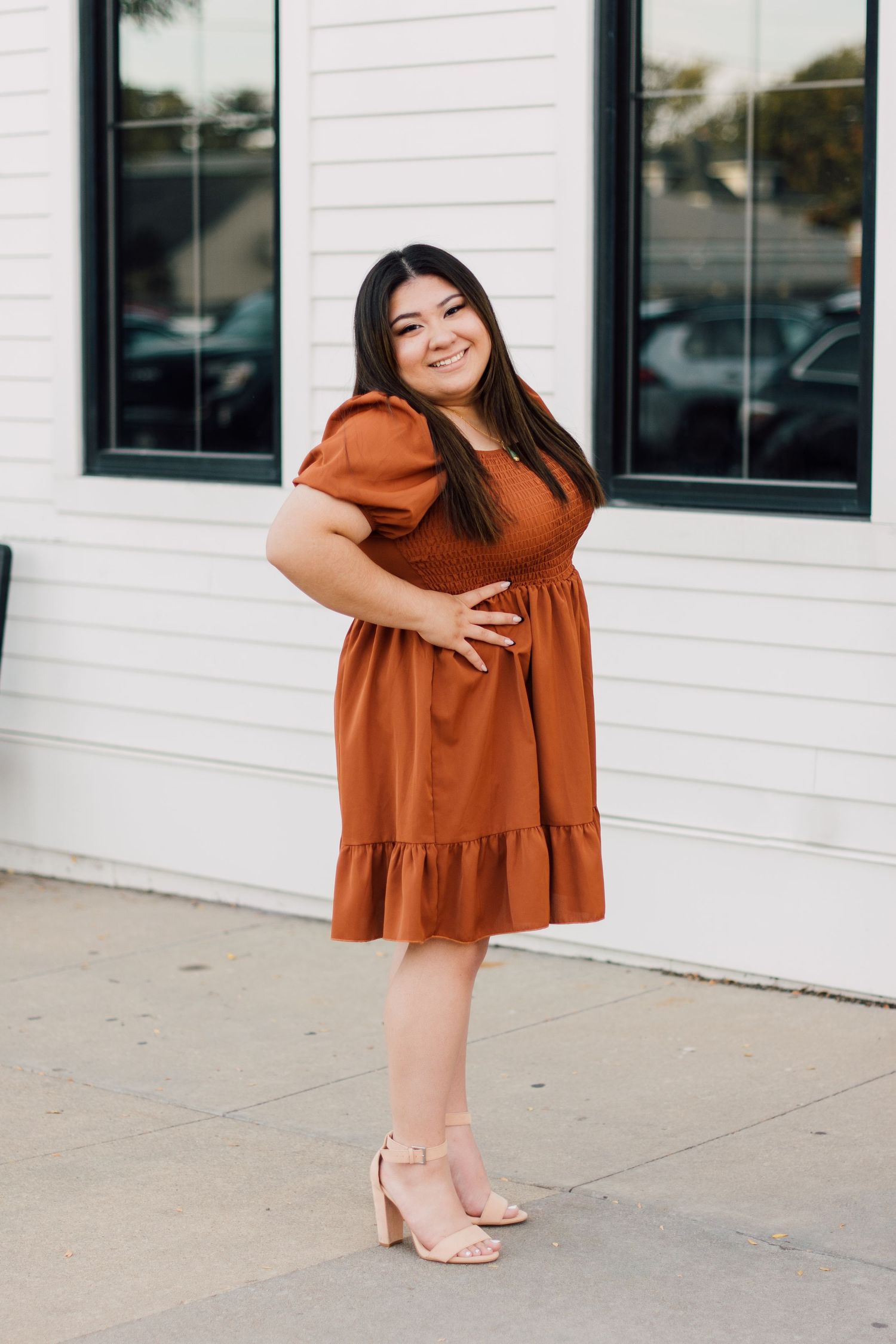 Playful fashion poses in a rust-colored babydoll dress against a white building exterior.