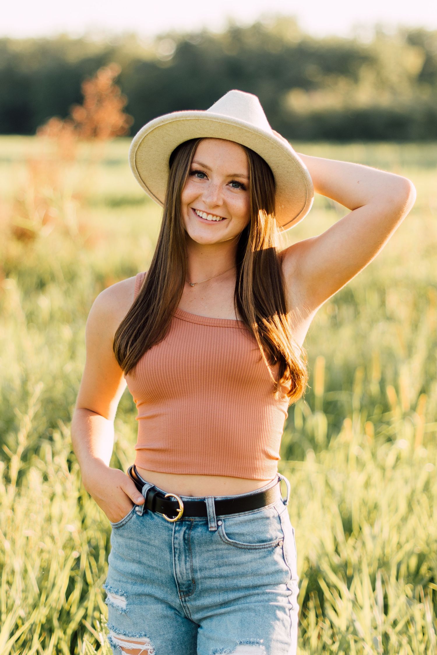 Summer outdoor photoshoot in wheat field wearing peach top, denim shorts and wide-brim hat.