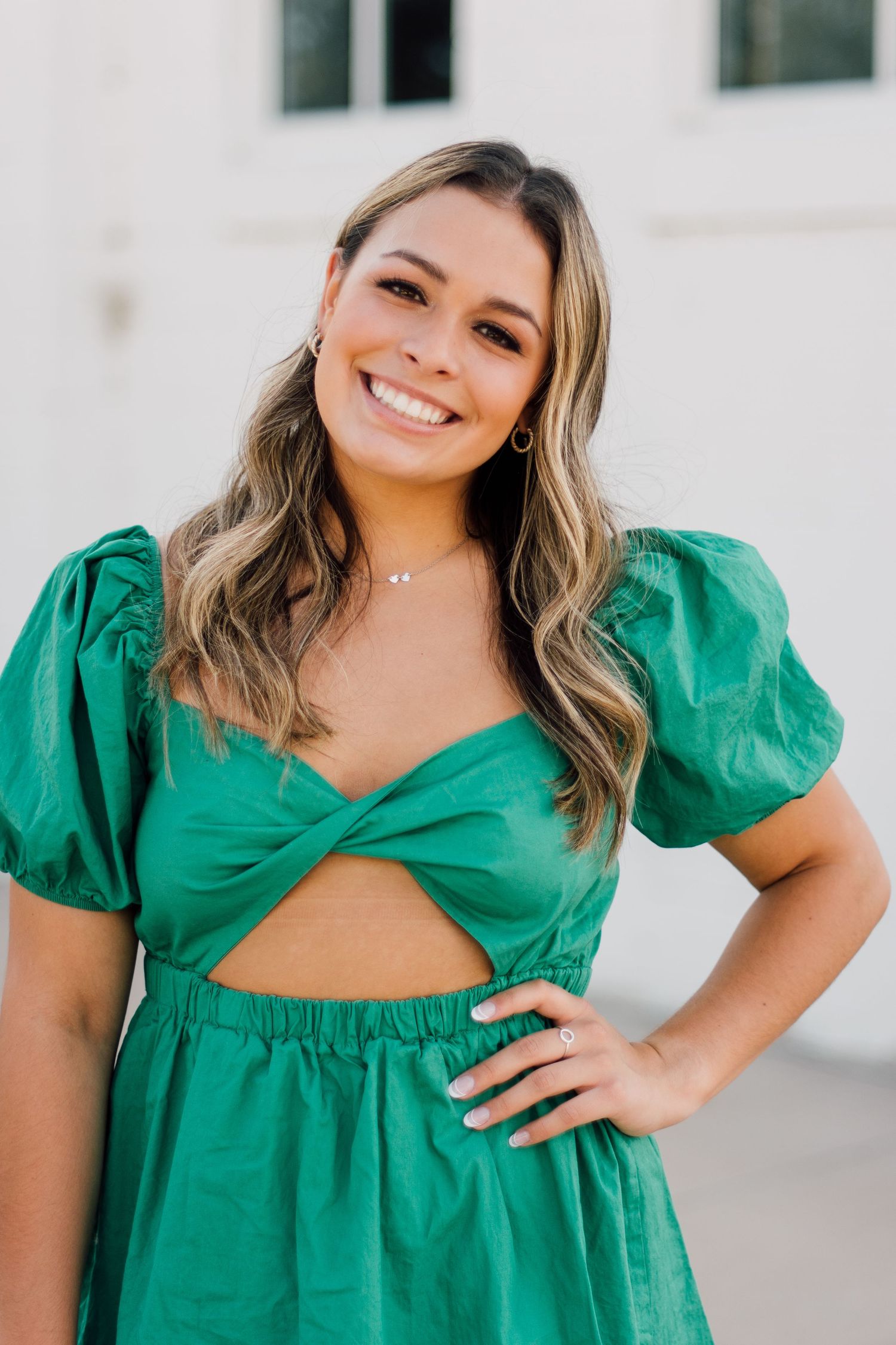 Portrait series in emerald green dress with puff sleeves against white wall.