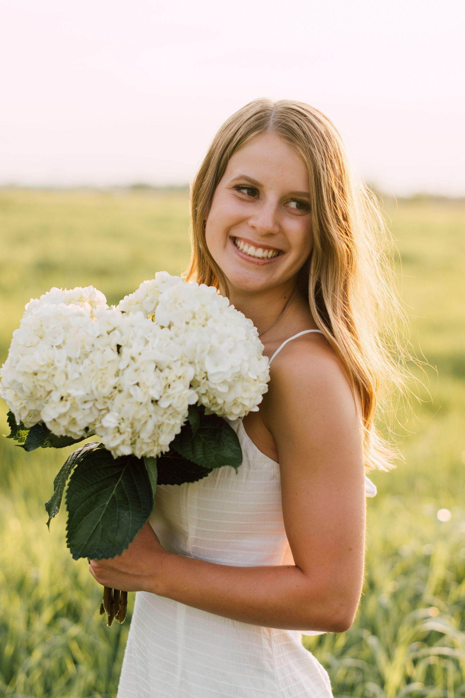 Summer portrait holding white hydrangea bouquet in sunlit field.