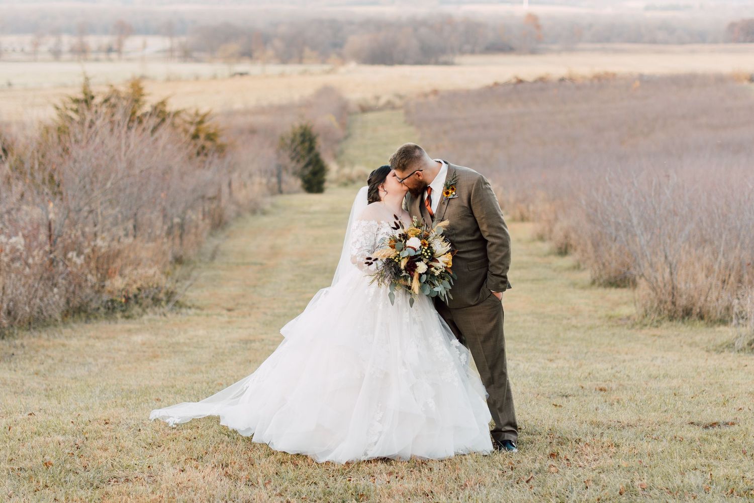 Wedding couple poses in rustic field during autumn season.