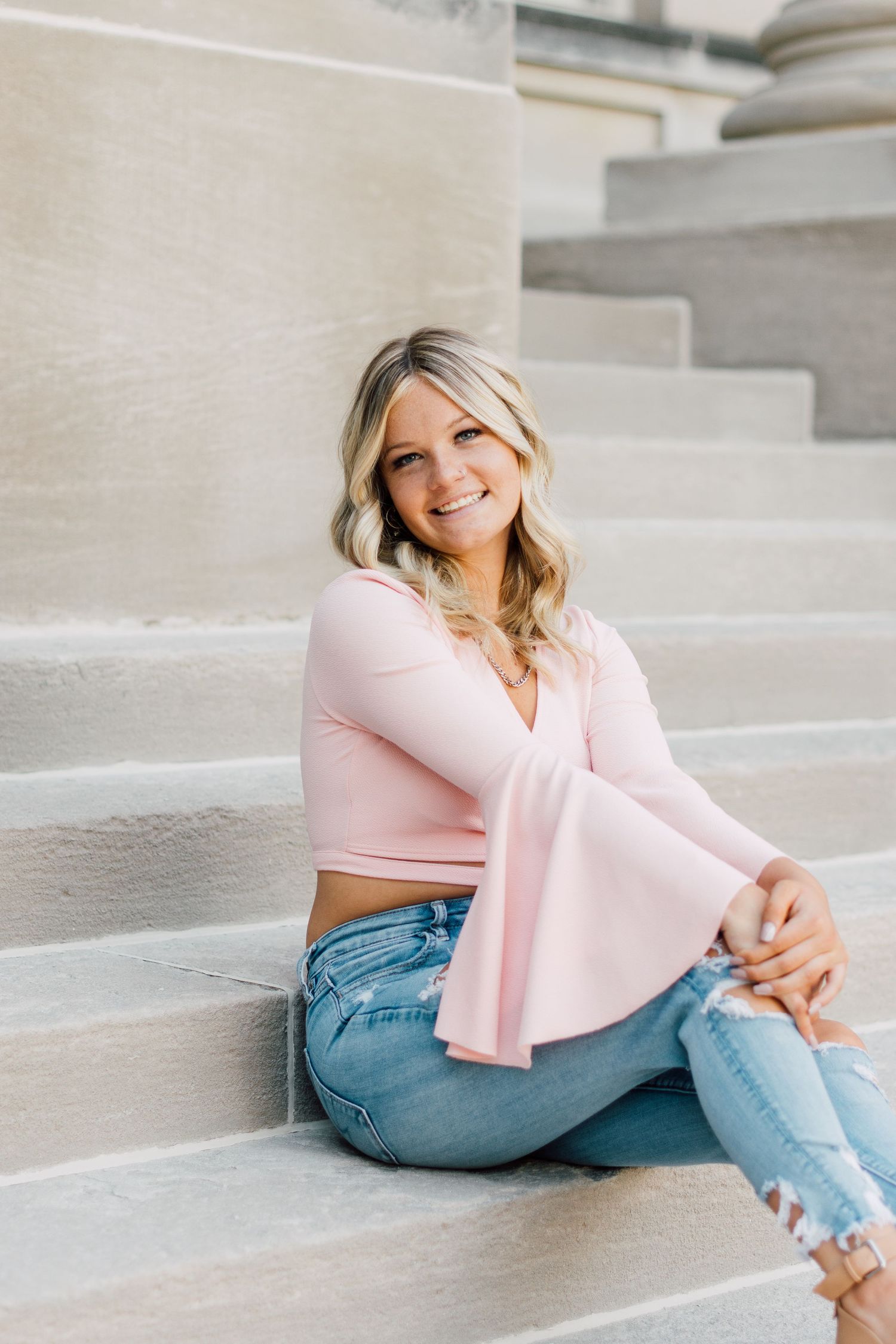 Casual portrait session on stone steps wearing pink sweater and distressed denim jeans.