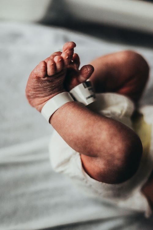 Close-up of tiny newborn baby feet with hospital ID bracelet on white bedding. Family photos Terre Haute union hospital
