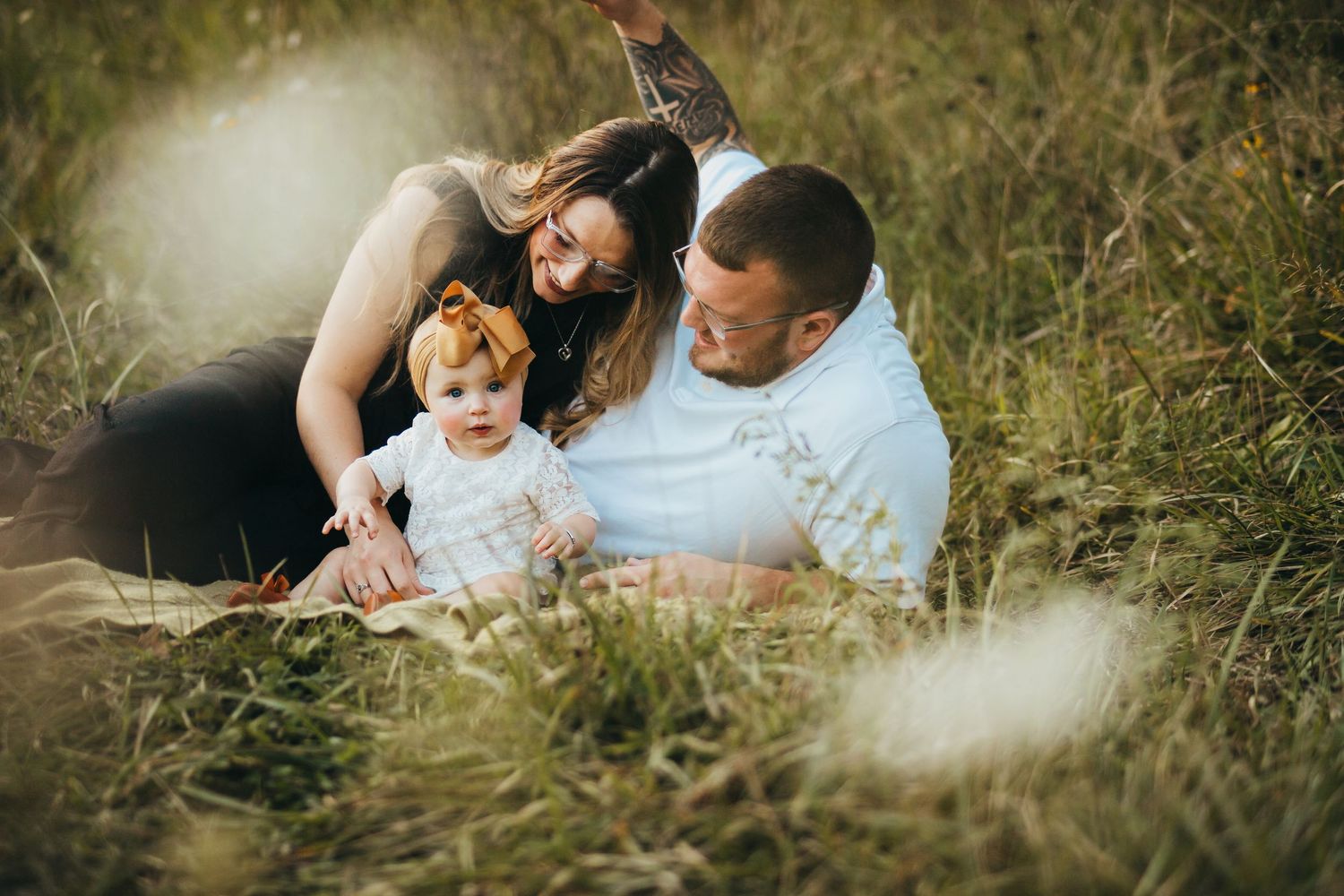 Family relaxing together in tall grass field on sunny afternoon with dreamy light filtering through.