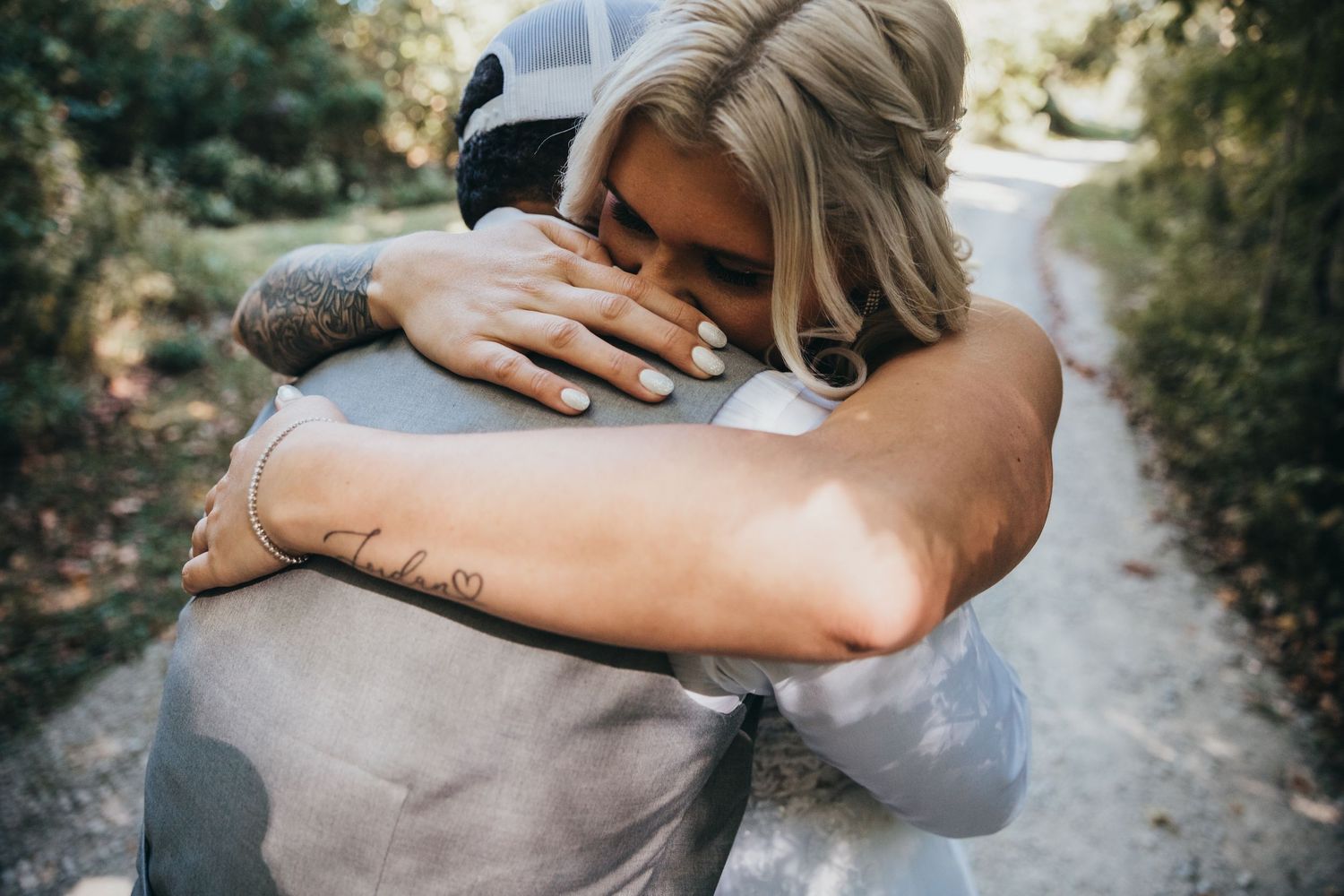 Two people embrace each other in a tender hug on an outdoor walking path surrounded by greenery. wedding couple pictures professionally