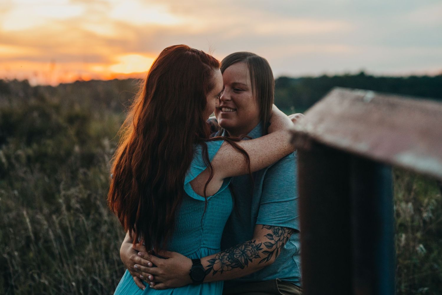 A loving couple in matching turquoise outfits embraces during golden sunset in a grassy field.