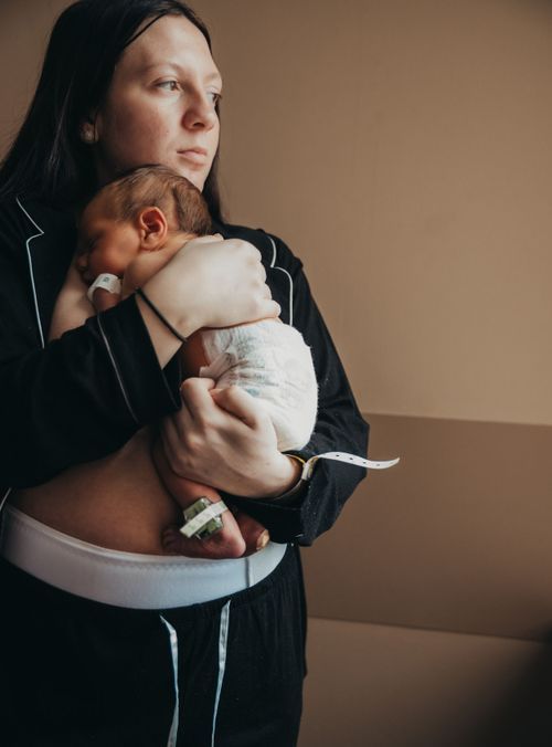 Tender intimate moment as mother cradles sleeping newborn baby against her chest in moody lighting. New mom photography Terre Haute Hospital