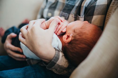 Newborn baby sleeping peacefully while being held in plaid shirt covered arms. Professional Family photos Clay county