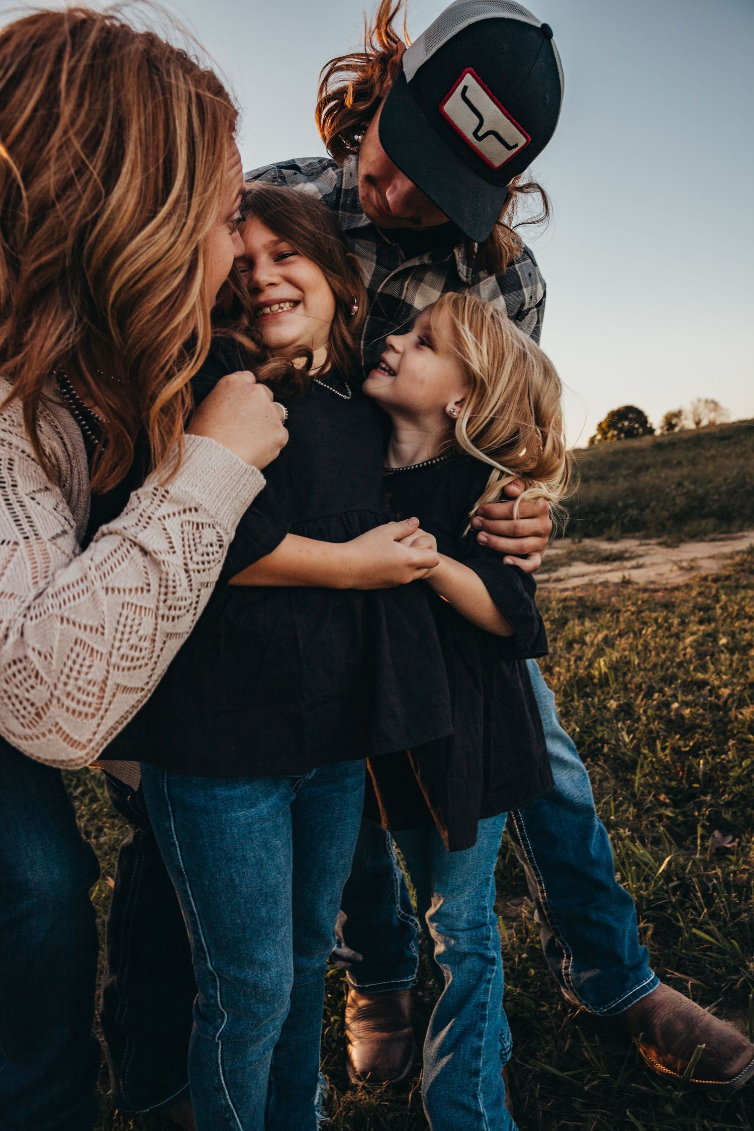 A candid family moment outdoors shows a group embracing and laughing together while wearing casual clothes at sunset.