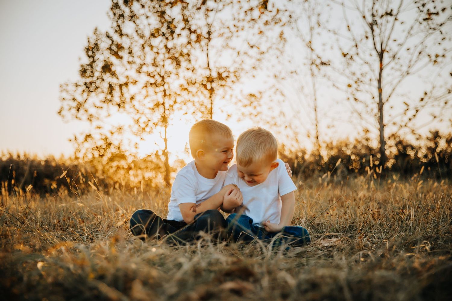 Two children sit together in a golden field at sunset while sharing a heartwarming moment.
