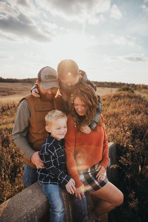 Family shares tender moment together at golden sunset in rustic field setting. Family photos Clay County