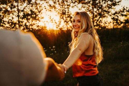 A person in a red tank top holds hands and spins during golden hour in a grassy field at sunset. engagement photographer pictures near vigo