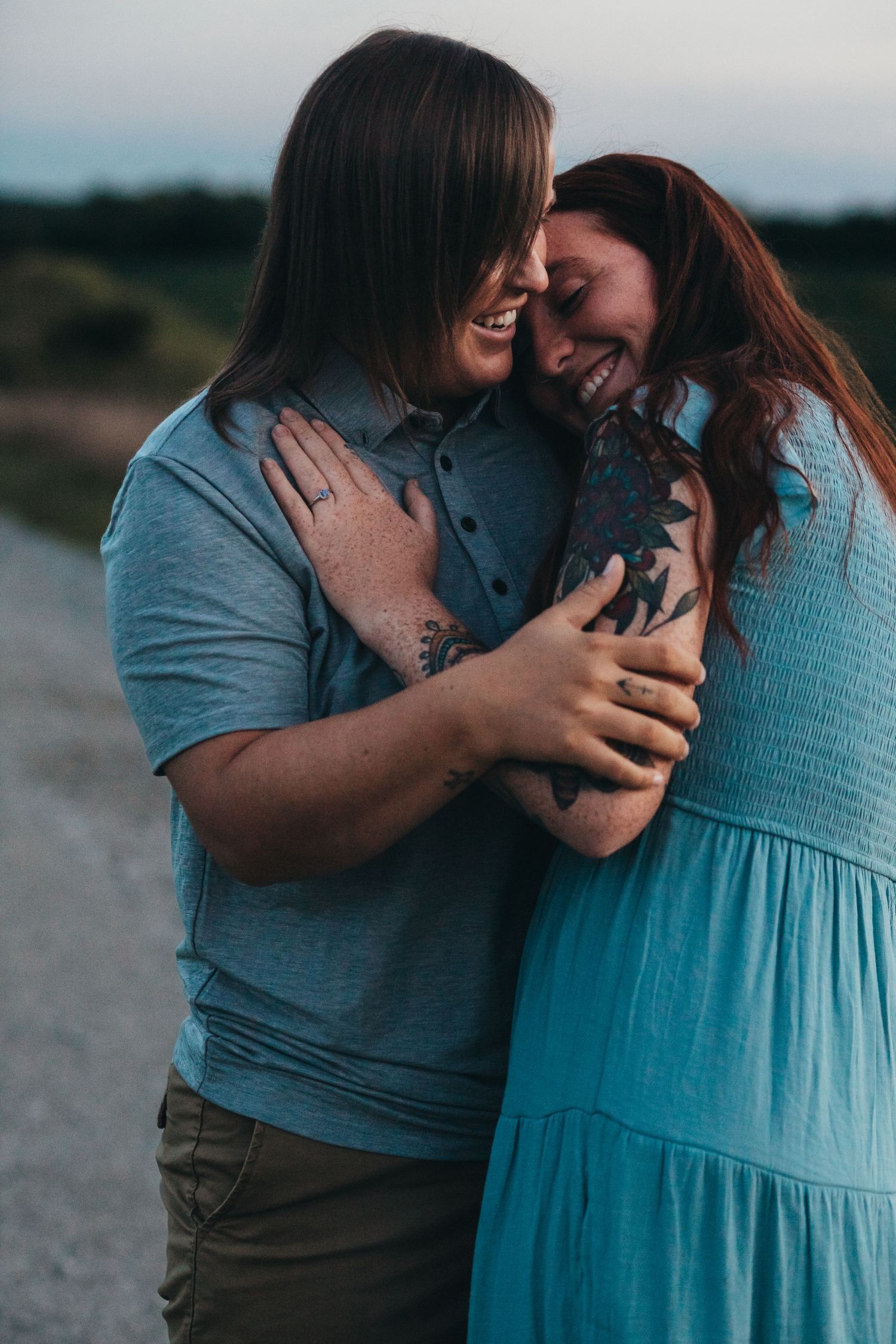 A couple shares a tender moment outdoors, wearing coordinating blue outfits while embracing and laughing together.