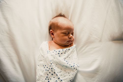 Newborn baby swaddled in white and gray polka dot blanket sleeping peacefully on light background. Newborn pictures Terre Haute