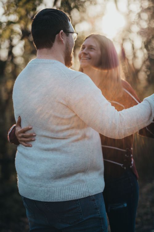 Romantic couple embracing outdoors during golden hour with sunlit trees in background. Engagement pictures near vigo county