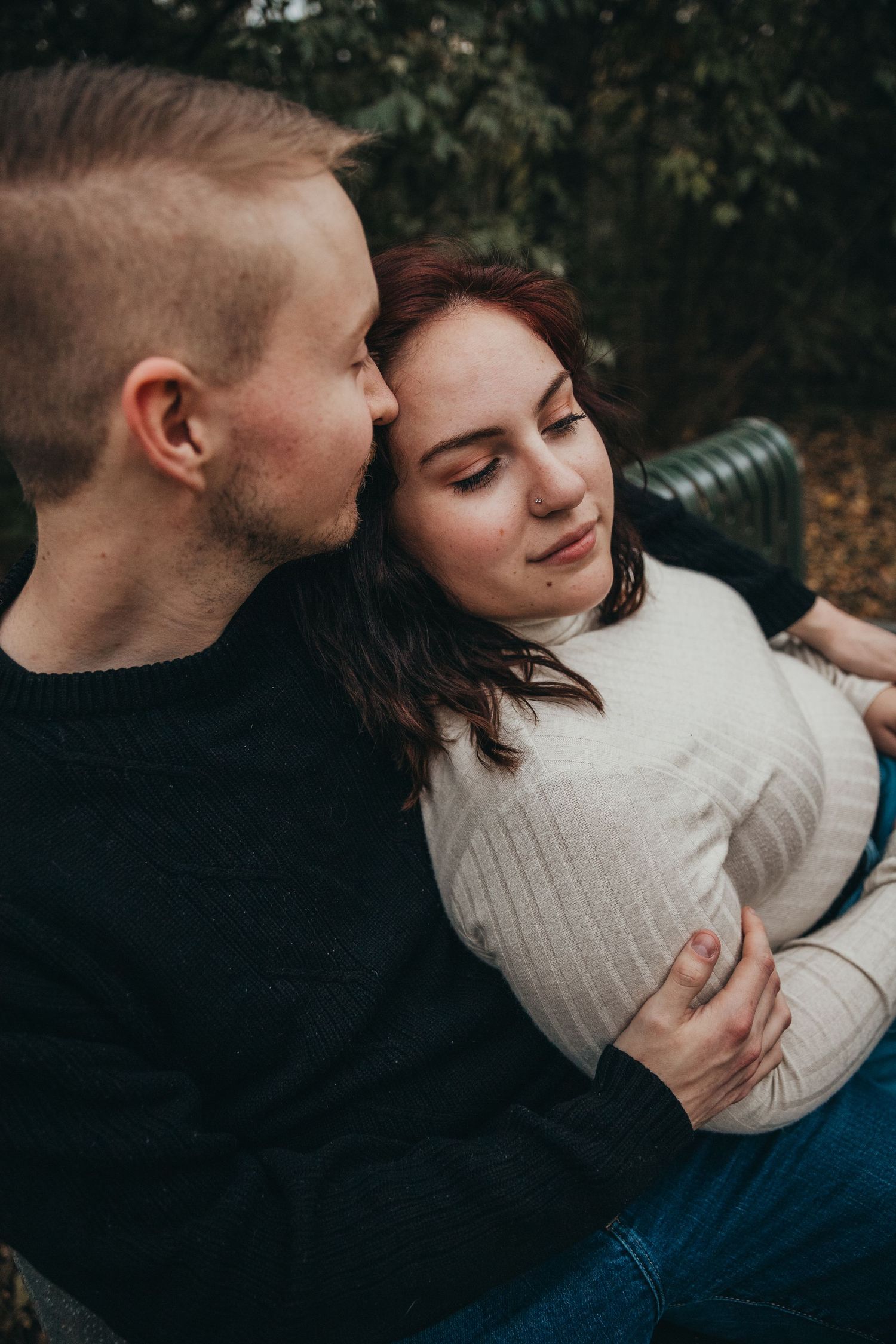 A couple in casual attire share an intimate moment while sitting outdoors in an autumn setting.