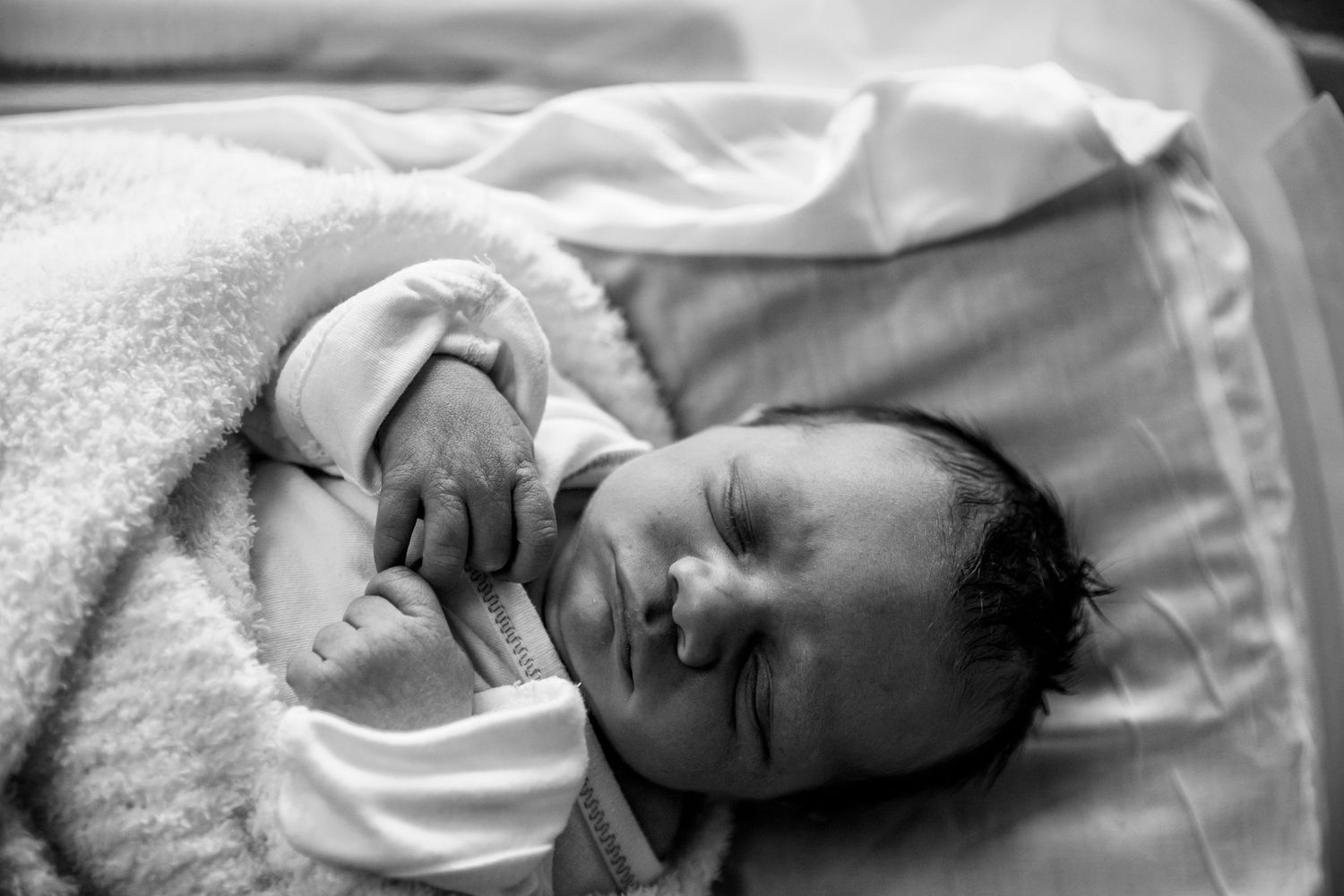 Peaceful newborn baby sleeping in black and white photography wrapped in soft blankets.