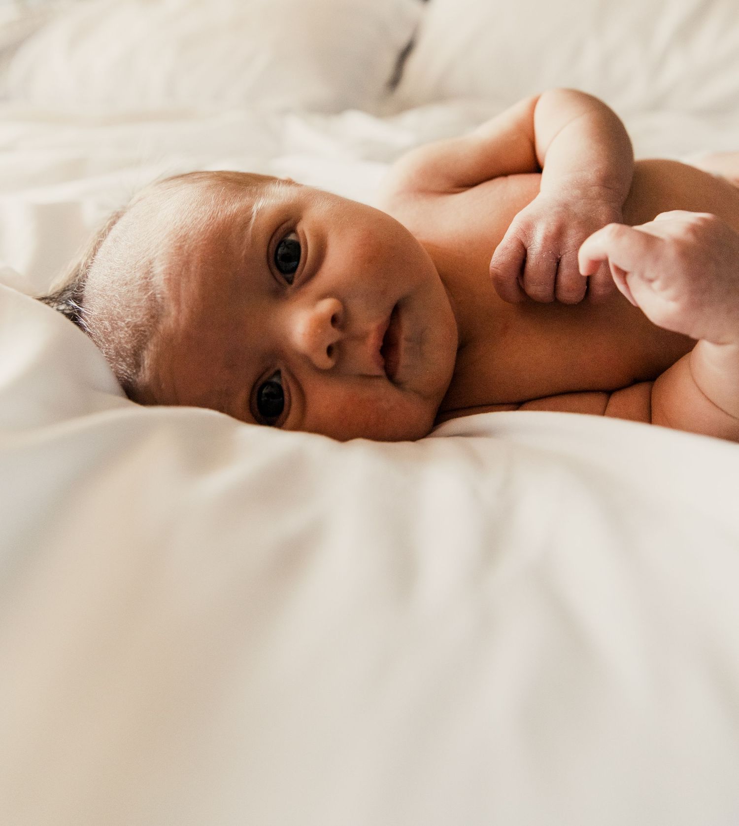 Terre Haute Baby Photography Newborn lying on soft white bedding while looking at camera with wide eyes.