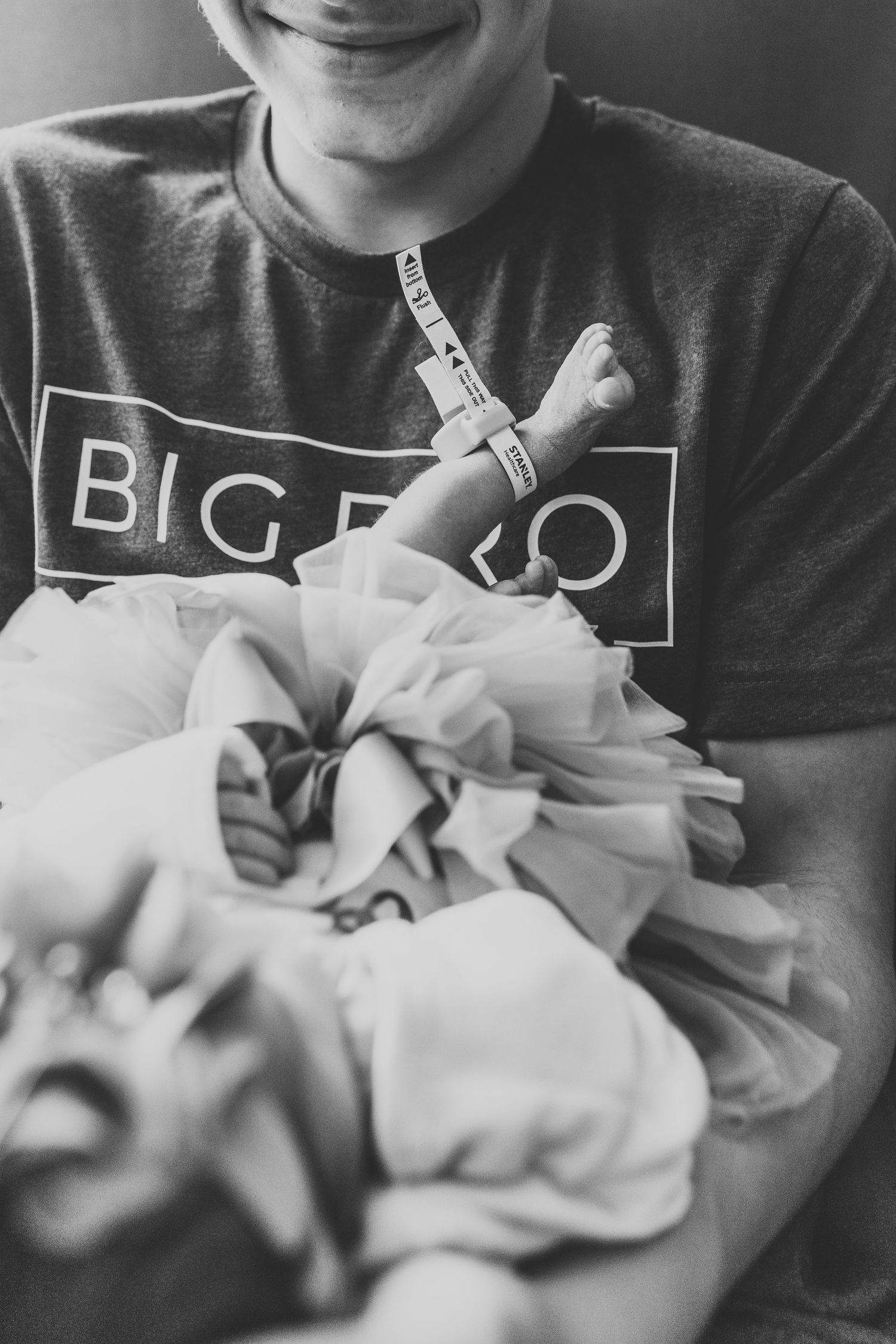 Someone wearing a Big Bro t-shirt holds a swaddled newborn wrapped in light fabric near sullivan county hospital