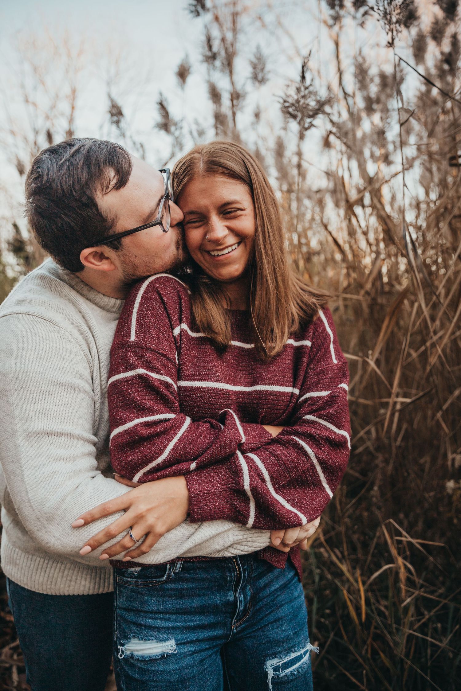 A couple embraces in tall grass during autumn, sharing a candid moment of joy and laughter.