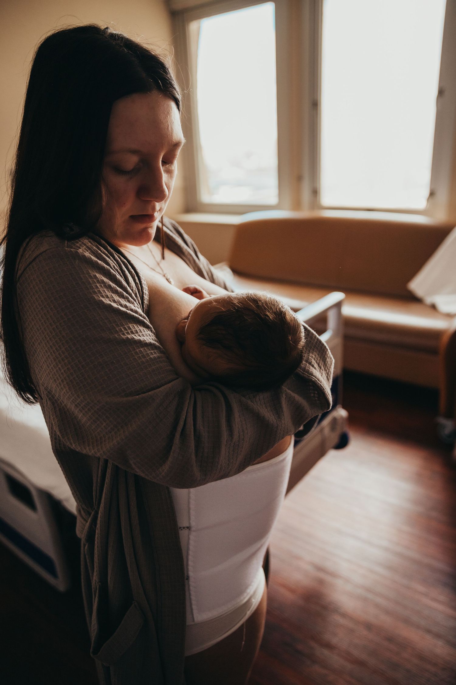 Union Hospital Terre Haute Newborn Photos. tender moment of parent and baby embracing by sunlit windows in a cozy room with hardwood floors.