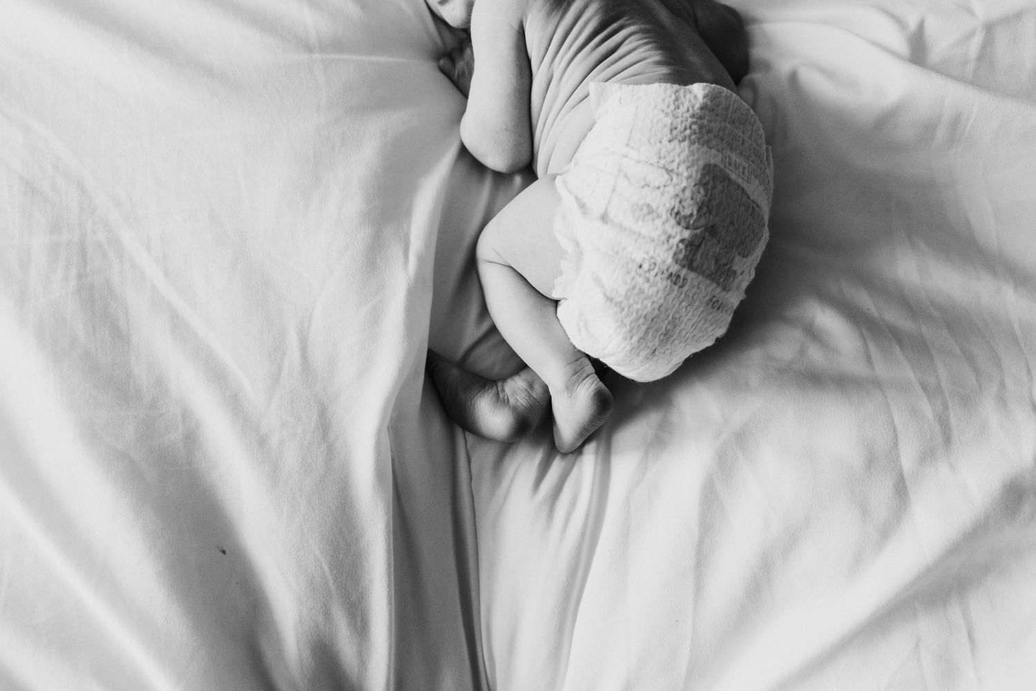 A sleepy dog lays comfortably in white bed sheets with paws resting near pillows.
