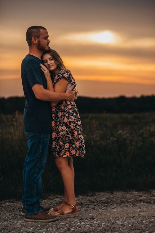 A couple embraces on a dirt path during a vibrant orange and golden sunset in a rural field setting. Couple photo session terre haute