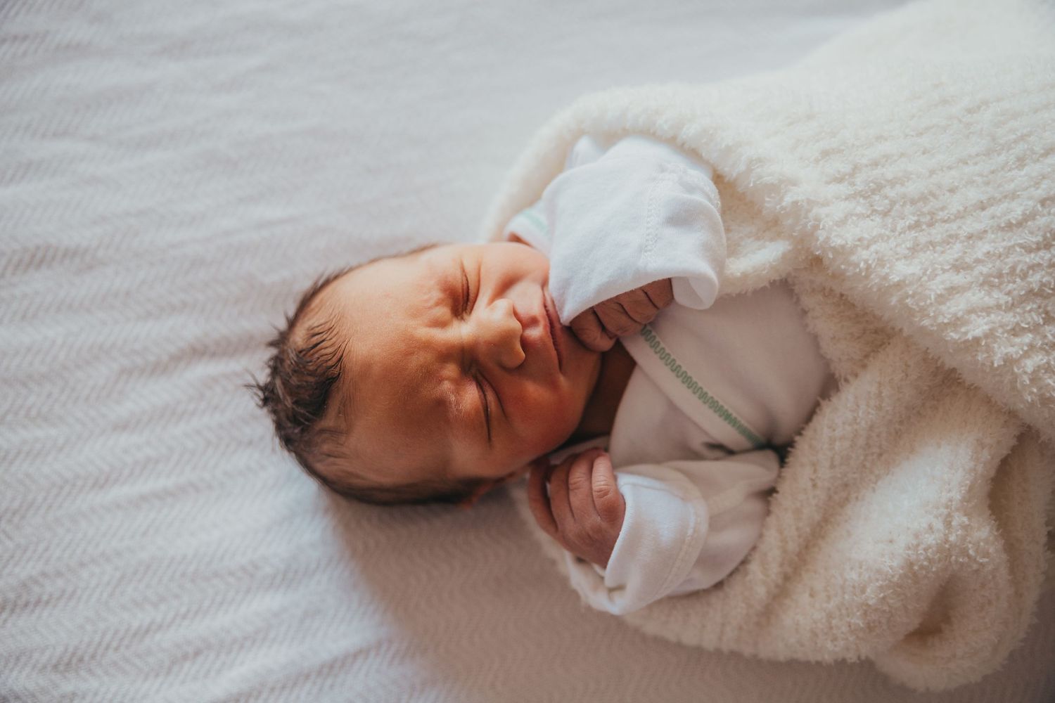 Newborn baby wearing white sleeps peacefully on soft white bedding. Union Hospital Terre Haute Newborn Photos