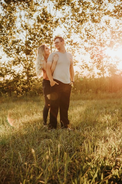 A couple embraces in a sun-drenched meadow during golden hour with trees softly glowing in the background. couple photos Vigo county