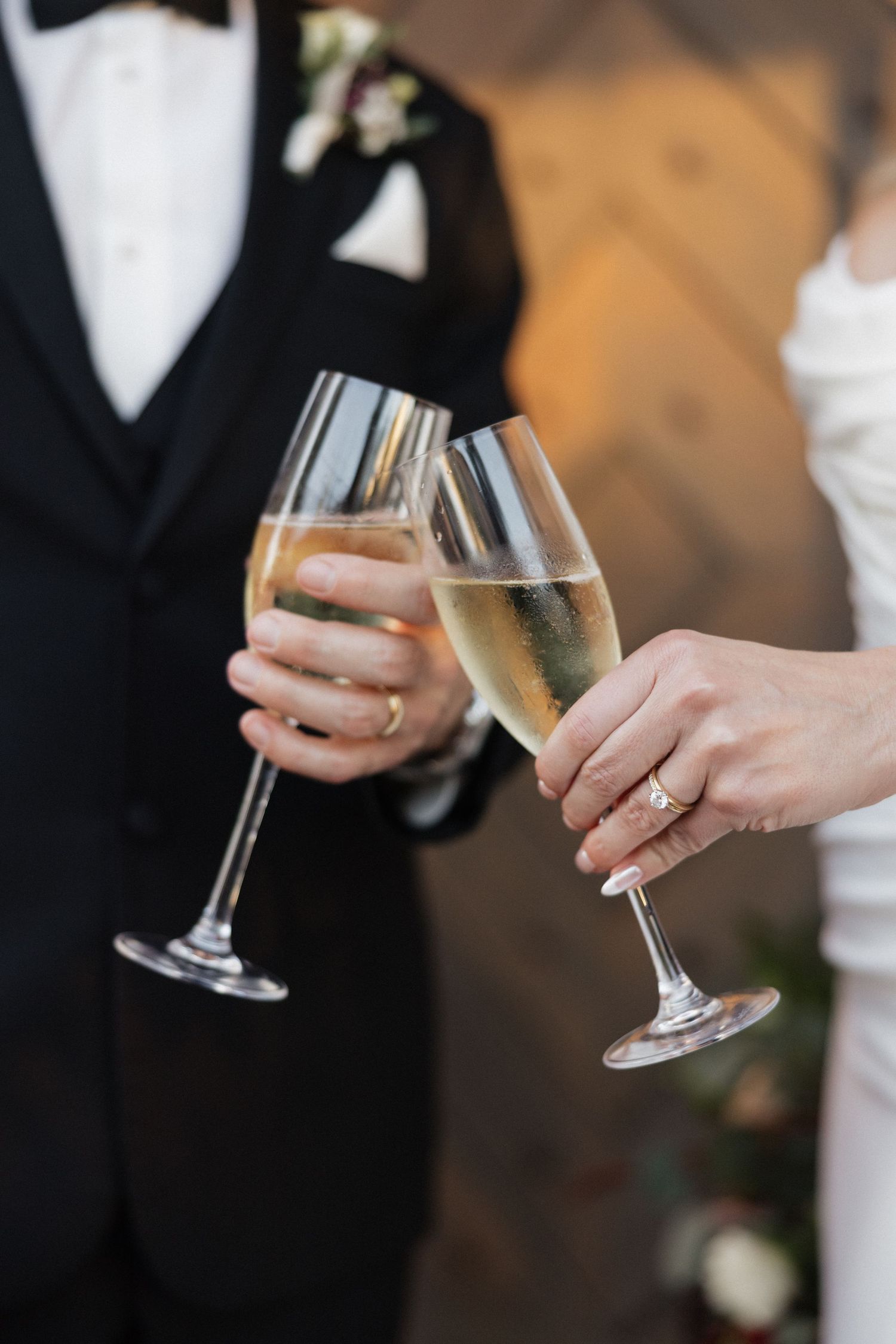 Two hands holding champagne glasses clink together in celebration at an elegant wedding reception.
