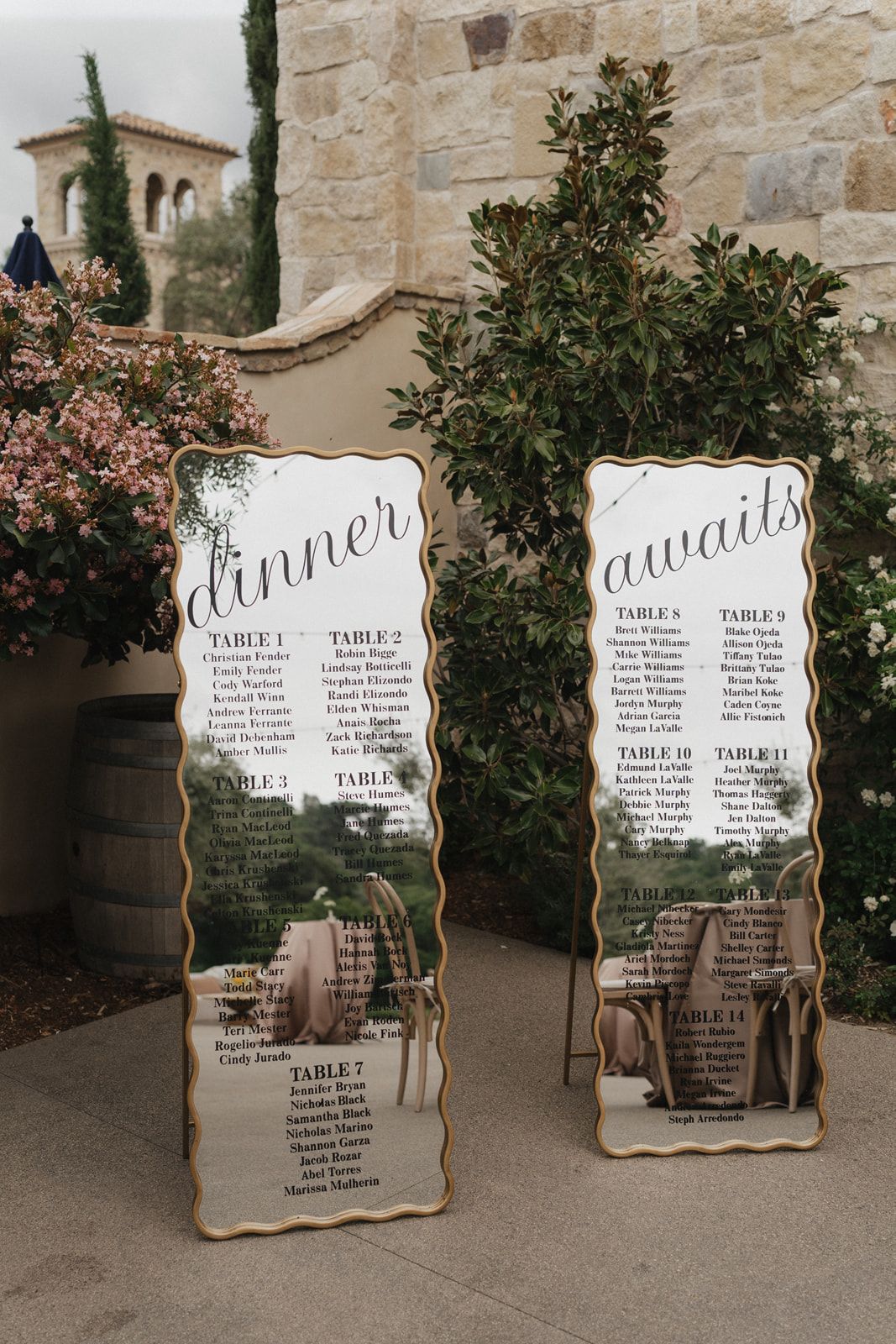 Elegant mirror seating chart displays for wedding reception with ornate gold frames against stone wall backdrop.